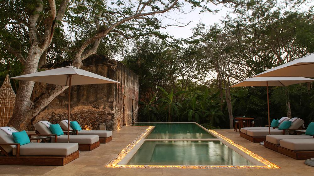 Chable Yucatan hotel pool area with illuminated rocks lining the pool with lounge chairs with umbrellas.