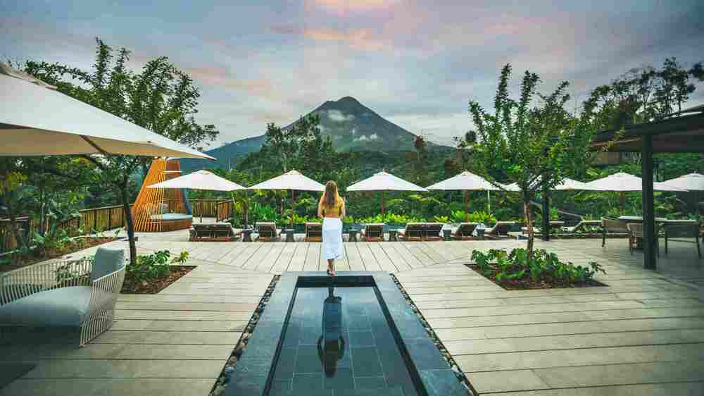 Guest walking along the pool area of Nayara Tented Camp with Arenal Volcano vista.