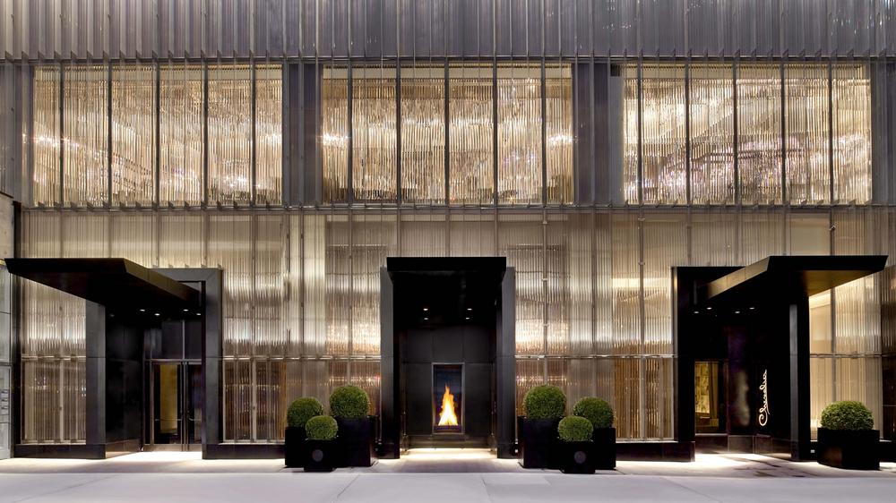 Exterior of The Baccarat Hotel with hotel with simmering glass to look like a sparkling chandelier with black entrance doors. 