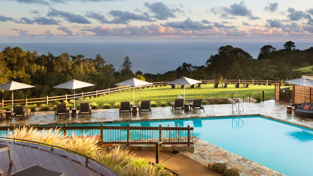 Pool area of Alila Ventana with poolside lounge chairs with white umbrellas and a panoramic view of the ocean. 