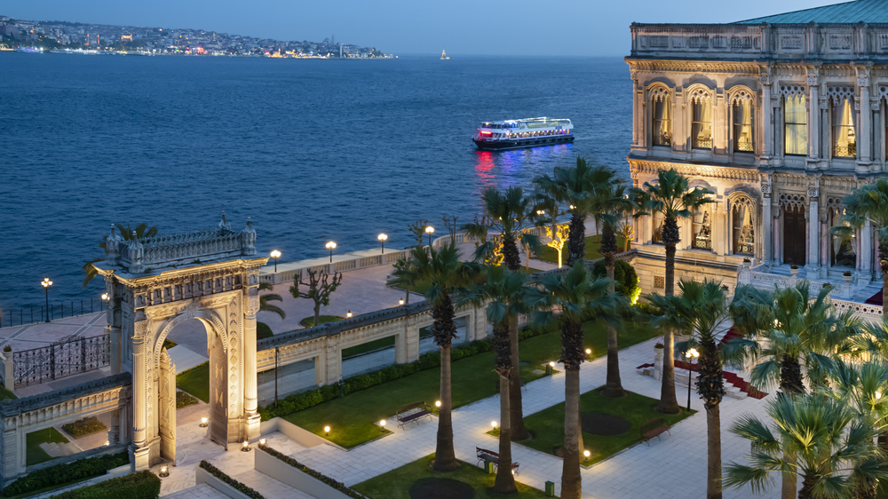 Exterior of Ciragan Palace Kempinski manicured courtyard with the ocean to the side. 