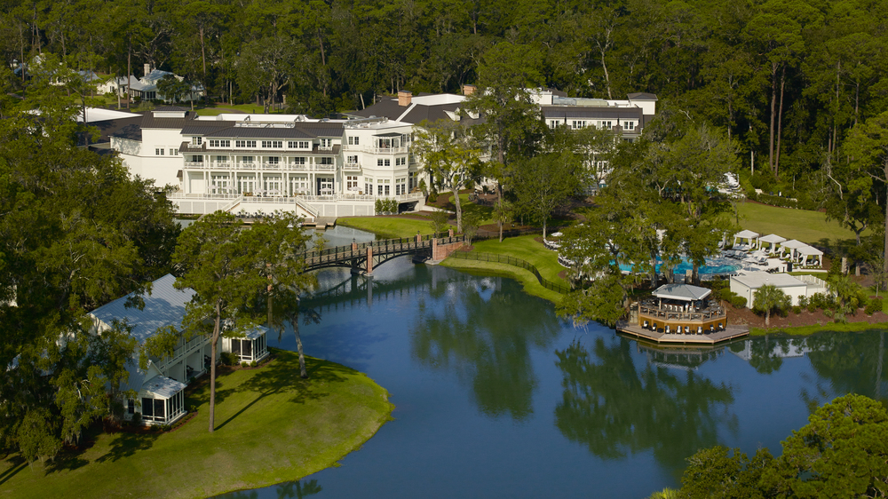 Montage Palmetto Bluff hotel grounds with large lake, bridge, pool area and main building surrounded by forest. 