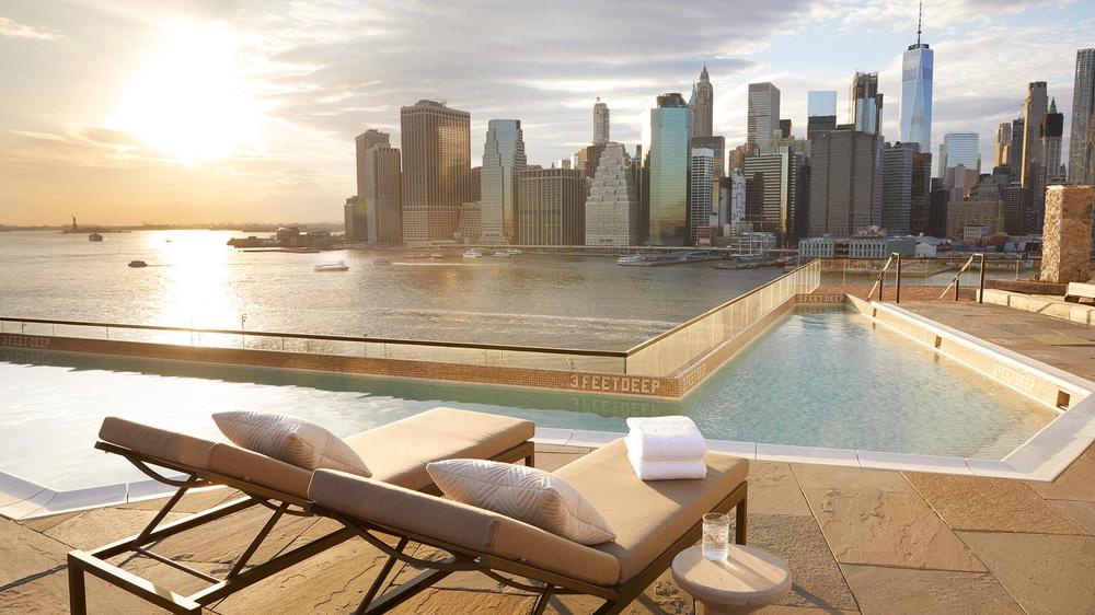 Rooftop pool area with a panoramic view of the Manhattan skyline and East River.