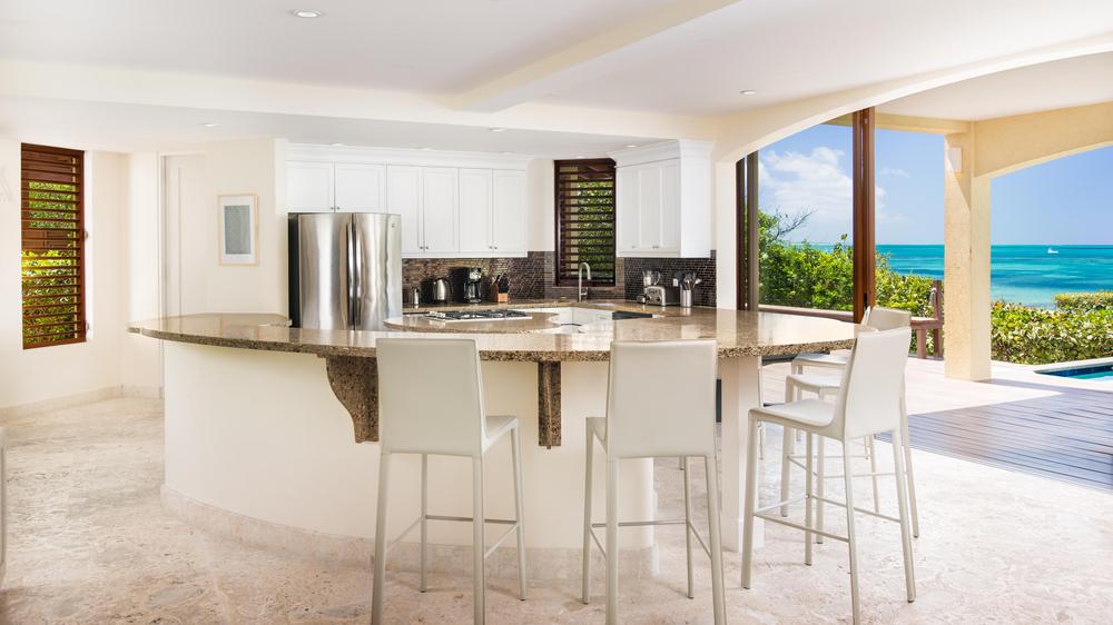 Luxury modern kitchen with large granite countertops with sliding glass wall that leads to outdoor lounge area with access and views of the ocean.