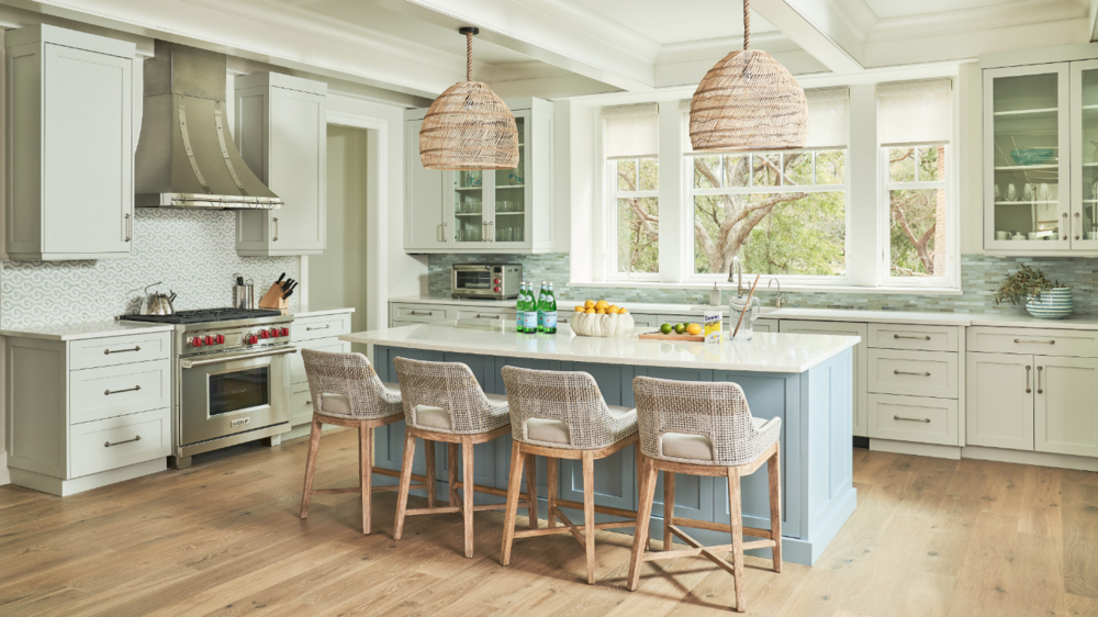 Luxury modern kitchen with stag green cabinets, with large island stocked with bottles of mineral water and fruit, and stainless steel appliances.