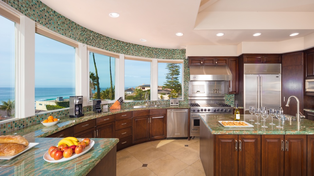 Luxury modern kitchen with granite counter tops and stainless steel appliances with plates of fruit and panoramic views of the ocean.