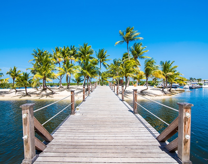 Dock overlooking a small island with palm trees and blue sky in Grand Cayman.