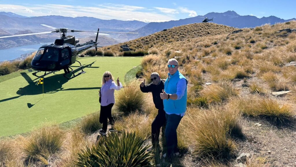 Inspirato members giving the camera a thumbs up while on the golf green next to a helicopter