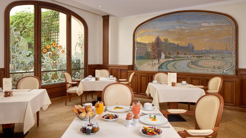 Indoor dining area with white linen table clothes with an assortment of pastries and a mural on one of the walls.