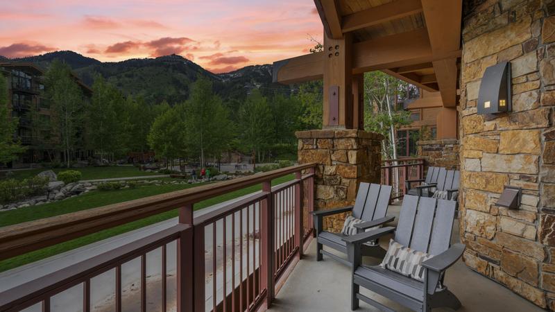 Balcony area with several chairs with views of a street below with a sunset above the mountains in the distance