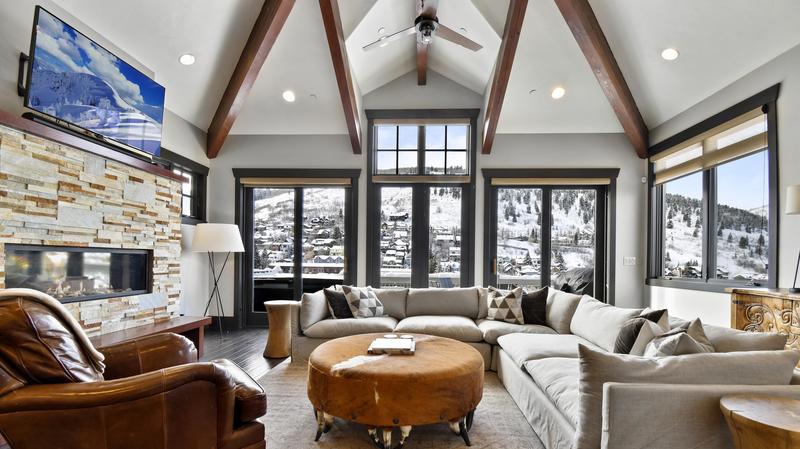 Tycoon living room with high vaulted ceilings with furniture arranged around a coffee table with a wall-mounted flat screen tv hanging above a fireplace.