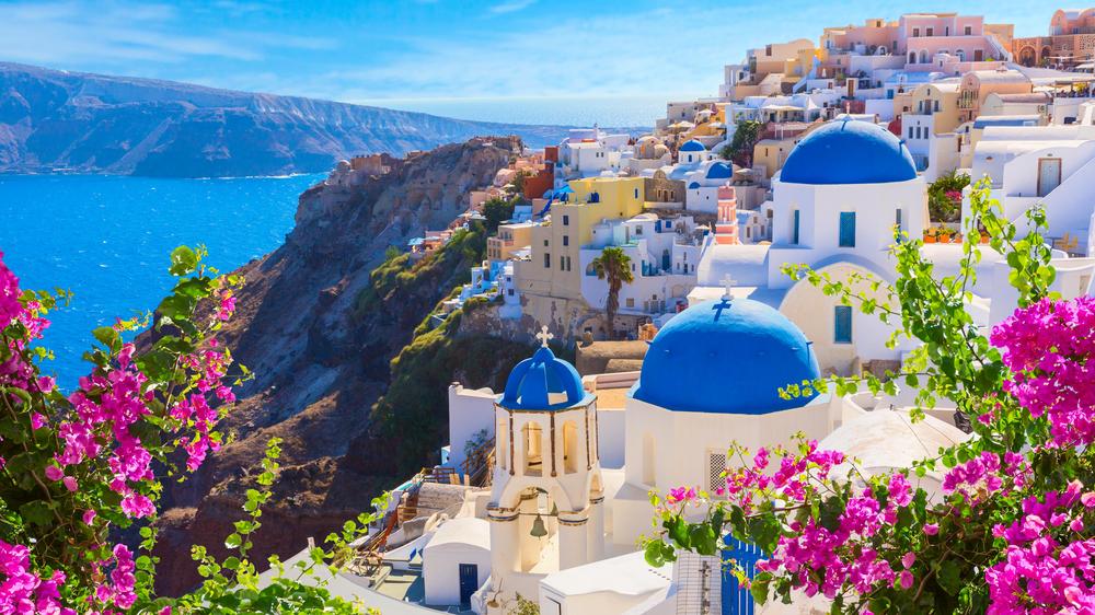 View of the cliffs of Santorini with the white and blue domed building with pink flowers surrounding the frame