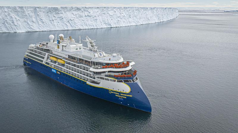 National Geographic Resolution ship in the water with a wall of ice behind it