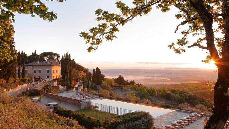 Rosewood Castiglion del Bosco estate with pool and main building with views of Tuscany during a sunset.