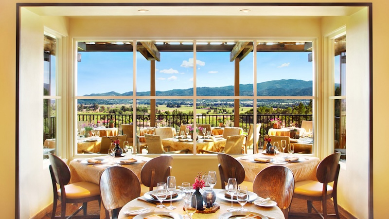 Auberge Du Solei indoor dining with a large window with views of the outdoor dining area and nearby vineyards.