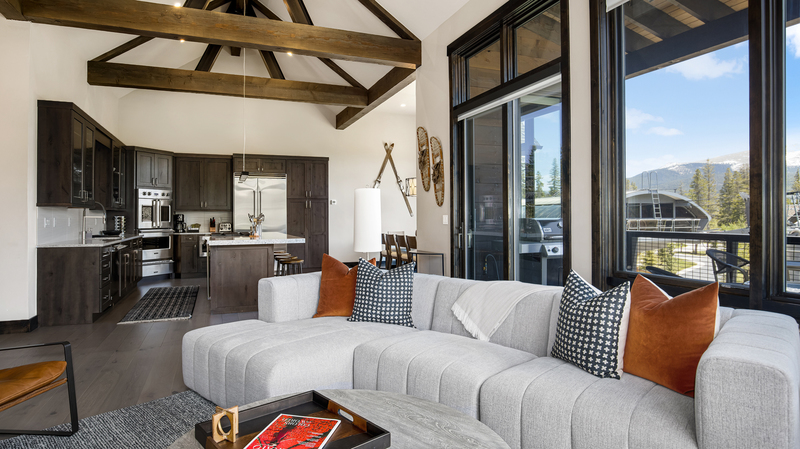 Living room of Cimarron with large white leather couch and kitchen area with high vaulted ceilings. 