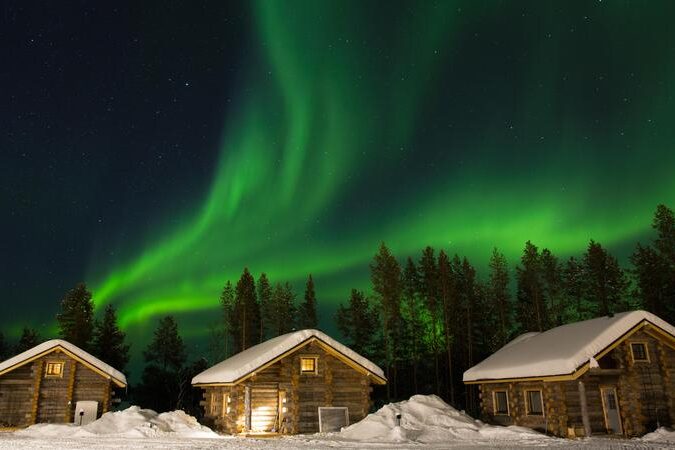 Northern lights illuminating over three winter cabins