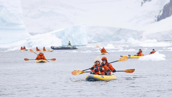 Inspirato members kayaking in the ocean with icebergs behind them