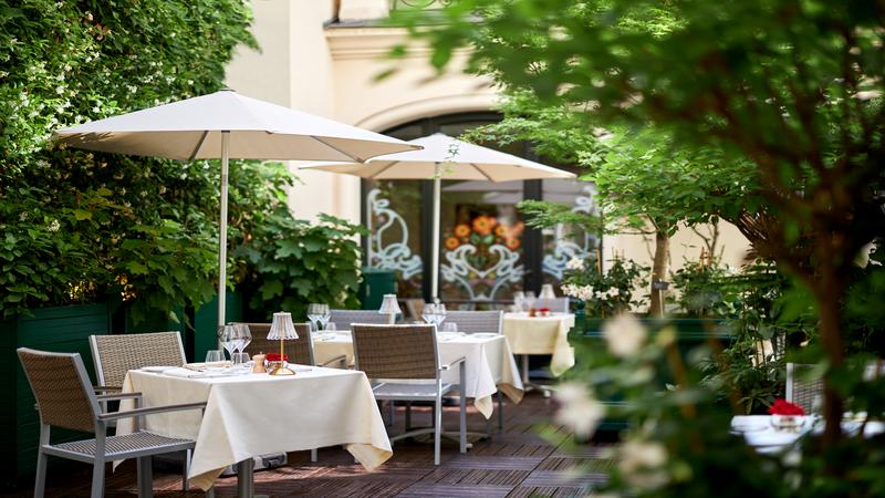 Outdoor dining area in a garden with umbrellas and fully set up white linen tables