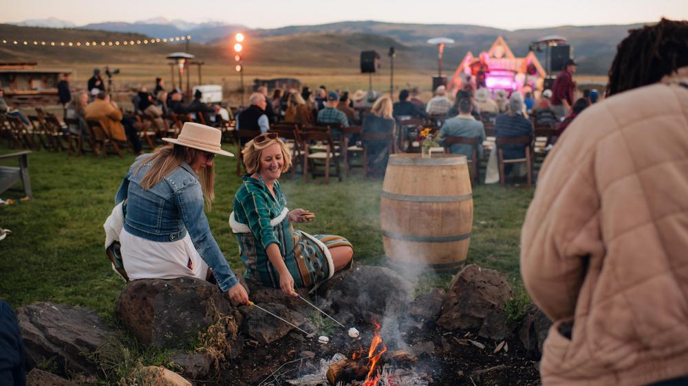 Inspirato members roasting marshmallows while an outdoor music performance happens behind them. 