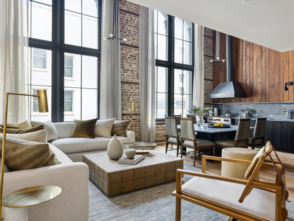 Bristow living room with cream furniture arranged around a coffee table with black kitchen with large island with chairs pulled up. 