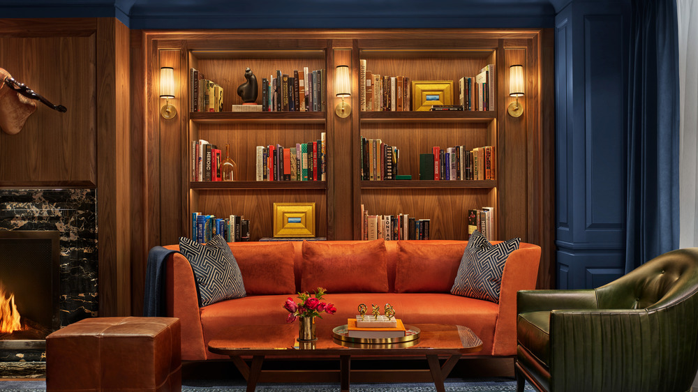 Lobby of Newbury hotel with a variety of leather and suede furniture with bookcase full of books and decor with a fireplace and blue walls. 