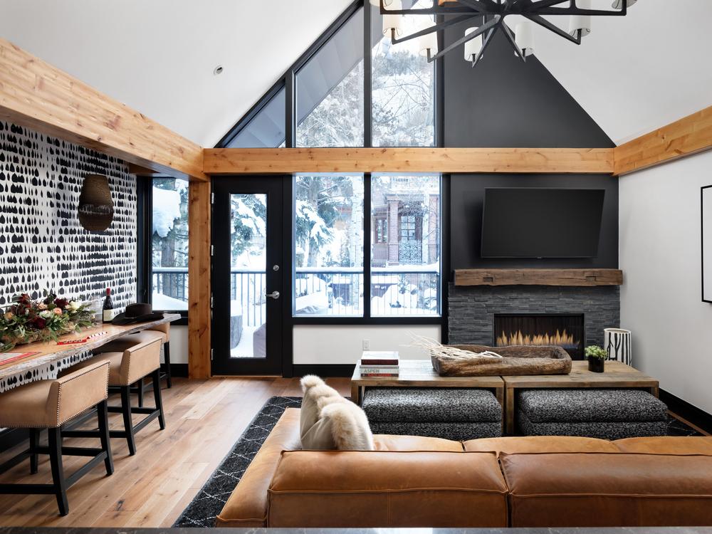 Copper Gulch living area with a-frame ceiling with large windows and leather furniture facing fireplace with wall-mounted flat screen tv hanging above.