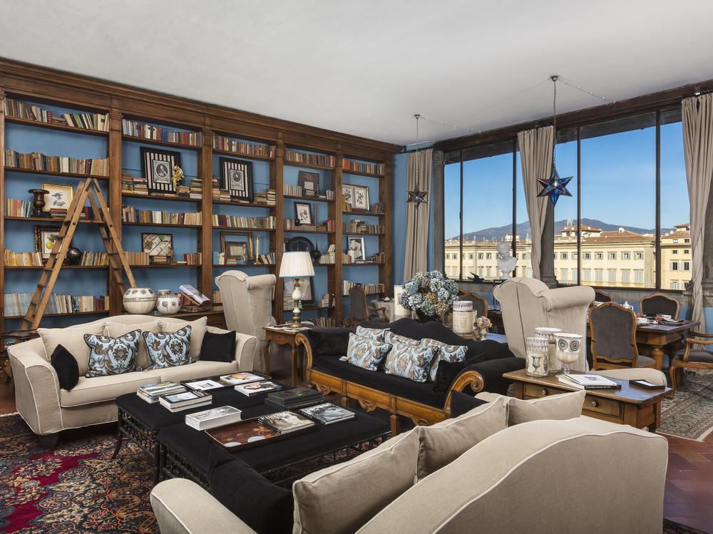 Foresteria Florentine living room with floor to ceiling bookcase with dining table and furniture arranged in a circle around a coffee table.