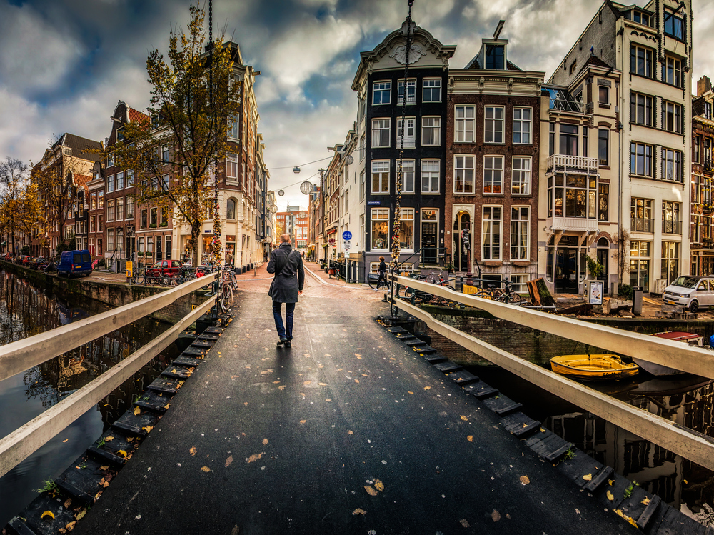 A person walking across a bridge over a Amsterdam canal with buildings lining the water