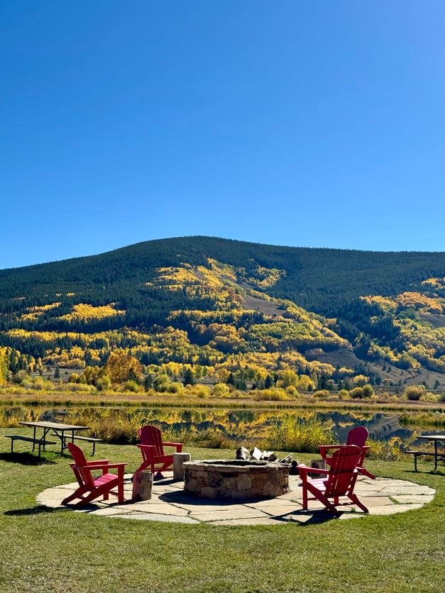 A fire pit with red chairs with a mountain vista with vibrant fall colors.