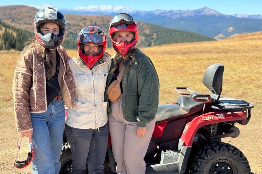 Three Inspirato members with helmets on standing in front of an ATV.