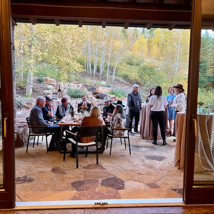 Inspirato members enjoying a welcome party on a stone patio with fall-colored aspen trees.