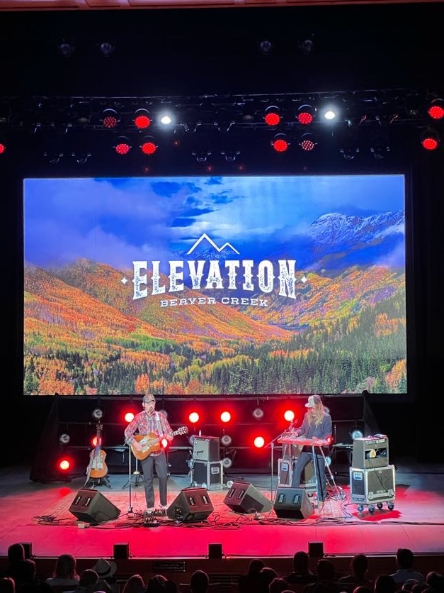 Two musicians on the Elevation Beaver Creek stage with red lights backlighting them.