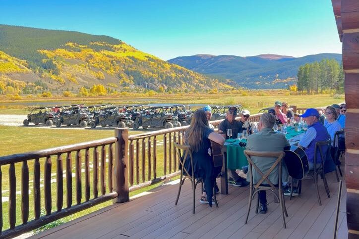 Inspirato members enjoying a lunch on a porch with a fleet of ATV's below and vibrant falls colors in the mountains.