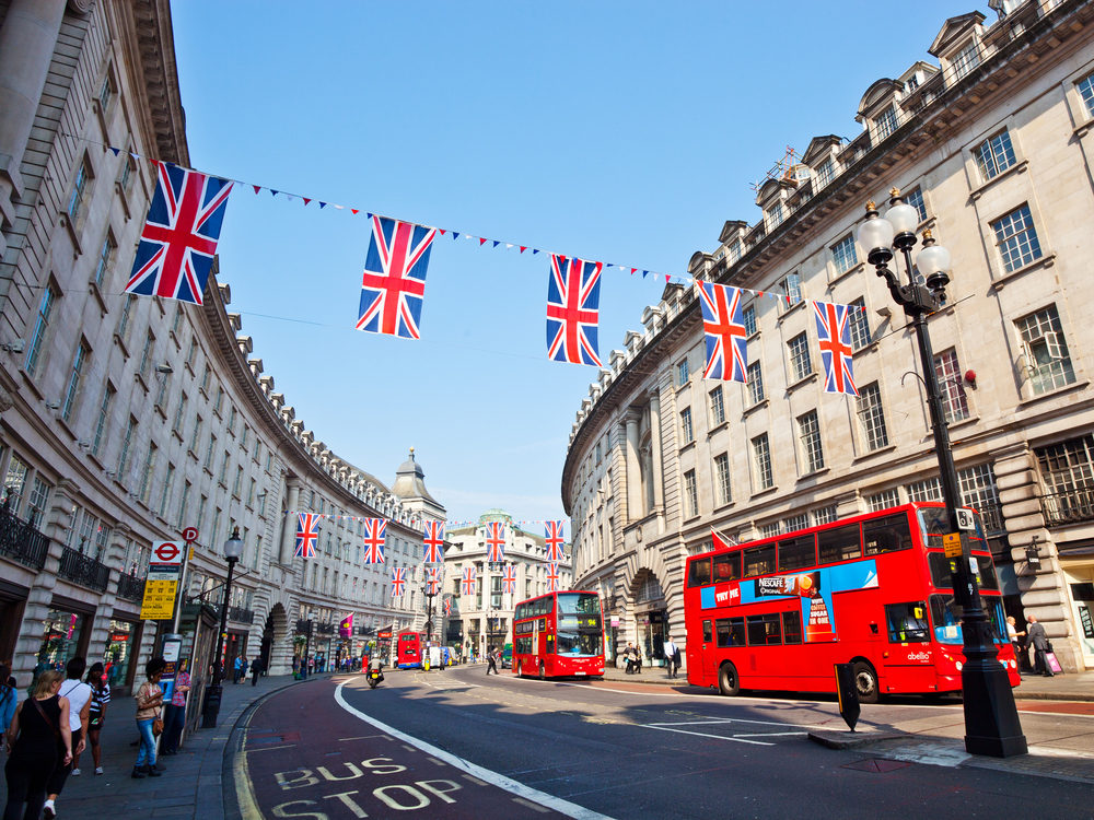 Street in London with double decker buses and England flags hung across street.