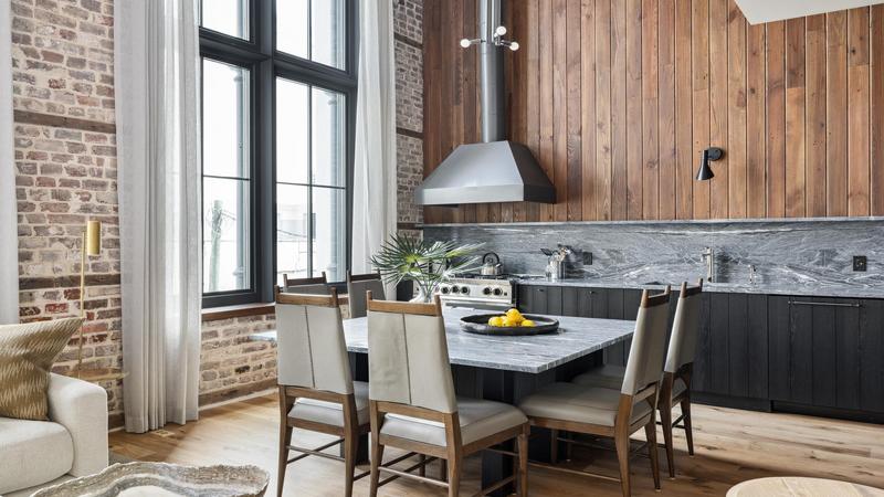 Rigney dining area with large square table that seats six with black and wood kitchen with stainless steel appliances. 