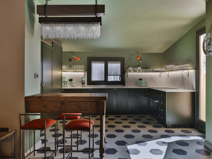 Garavani kitchen with patterned tile flooring, small elbow bar with two red bar stools, and black cabinets.