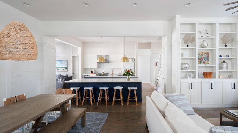 Magnolia great room with dining table with benches on each side with kitchen with blue colored island with stools pulled up and white cabinets.