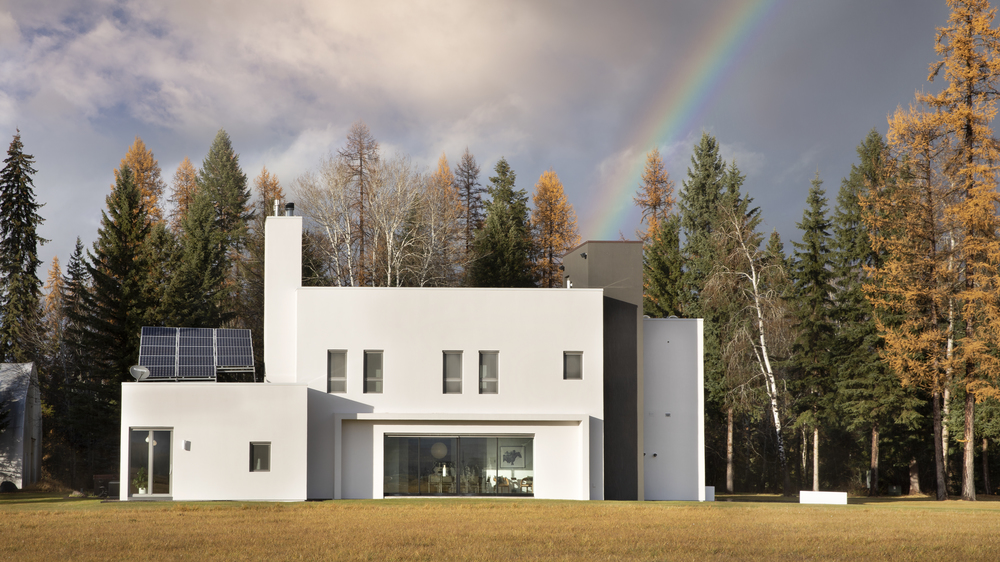 All-white exterior of the Stillwater Retreat home with autumn colored trees and a rainbow above the home. 